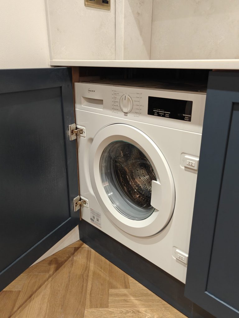 Integrated washing machine behind cabinet door in Hague Blue shaker kitchen