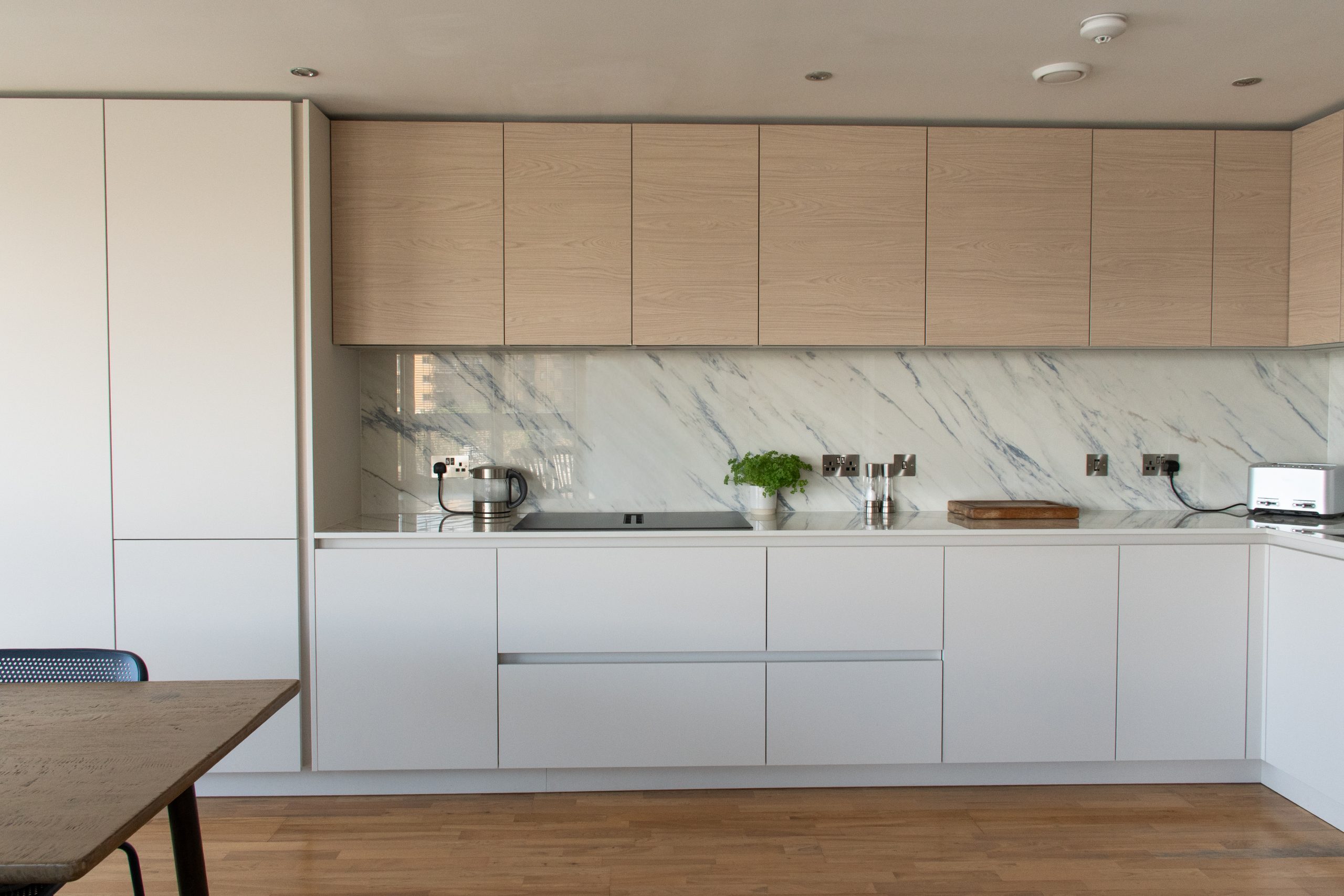 Side angle of porcelain and cashmere handleless kitchen with integrated appliances, Victoria Kitchens, Greenwich SE10