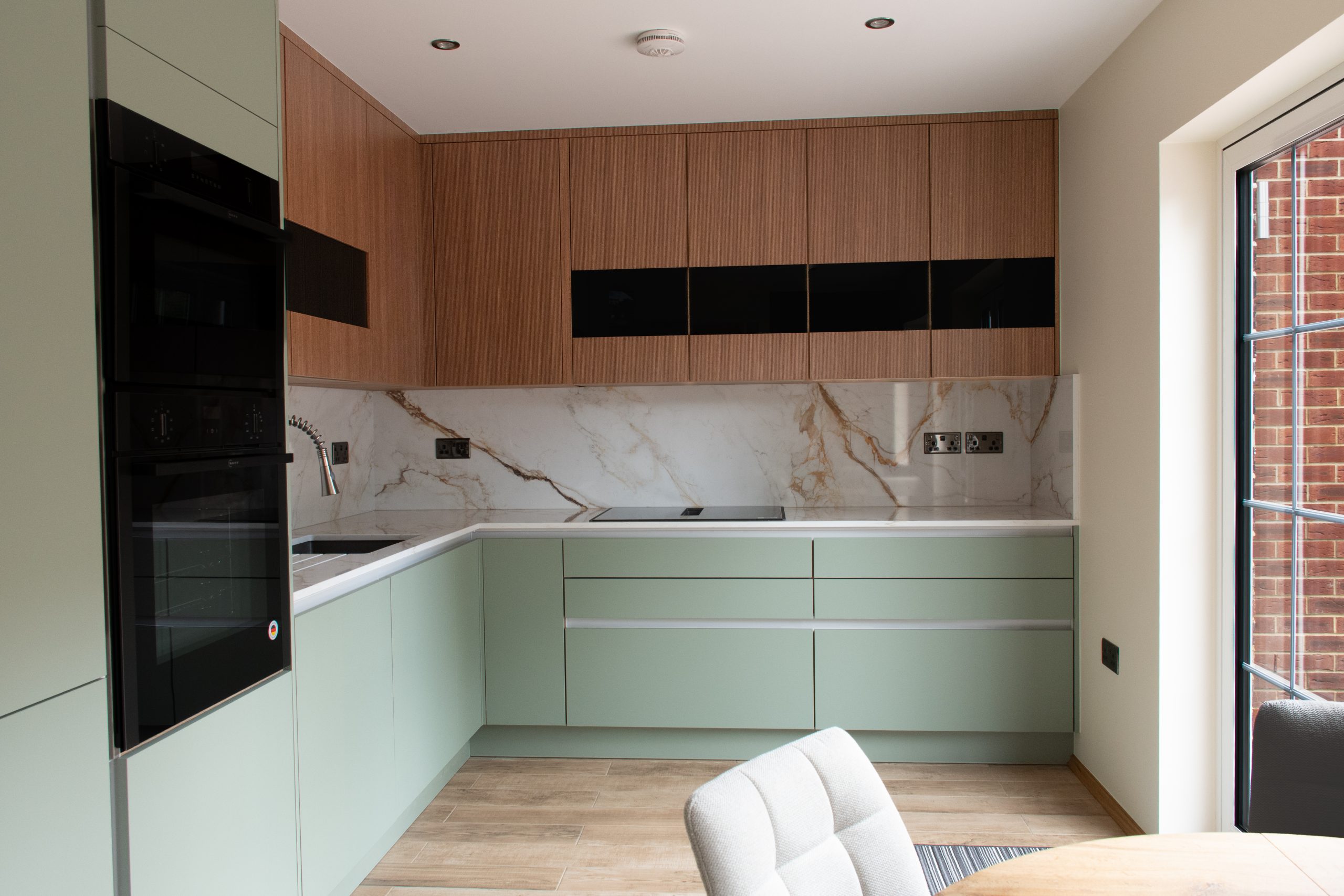 Wide view of sage green and smoked oak modern handleless kitchen, Eltham SE9, designed by Victoria Kitchens