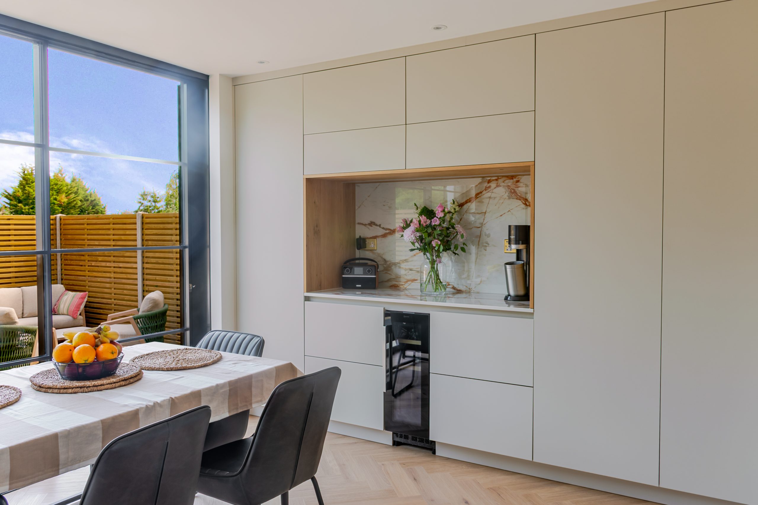 Wide angle showing wine cooler, open display niche, splashback, worktop and garden view through bifold doors, Rotpunkt kitchen, Victoria Kitchens