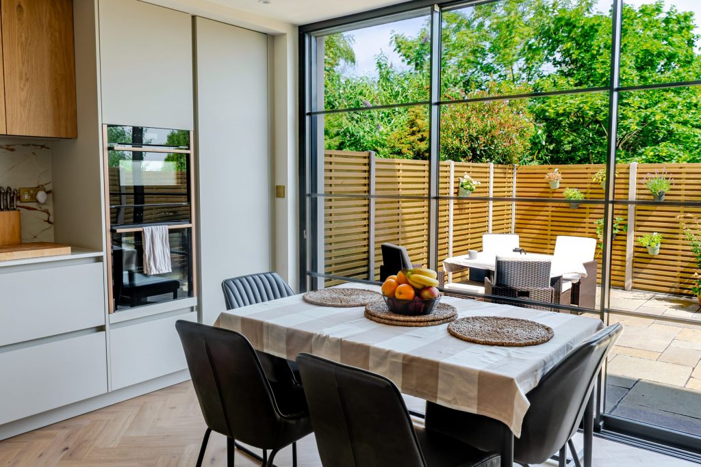 Wide angle of Rotpunkt kitchen showing twin Neff ovens, cabinetry, garden view and dining table with fruit bowl, Victoria Kitchens