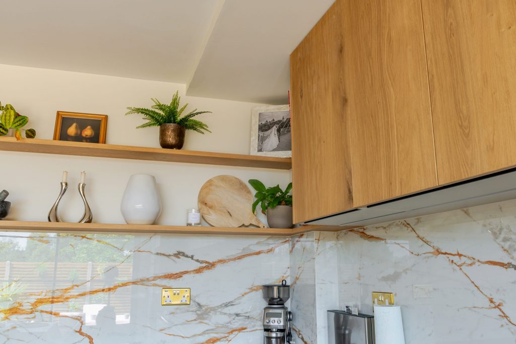 Close-up of Rotpunkt oak veneer cabinet corner with Dekton splashback and styled floating shelf brackets with plants, Victoria Kitchens