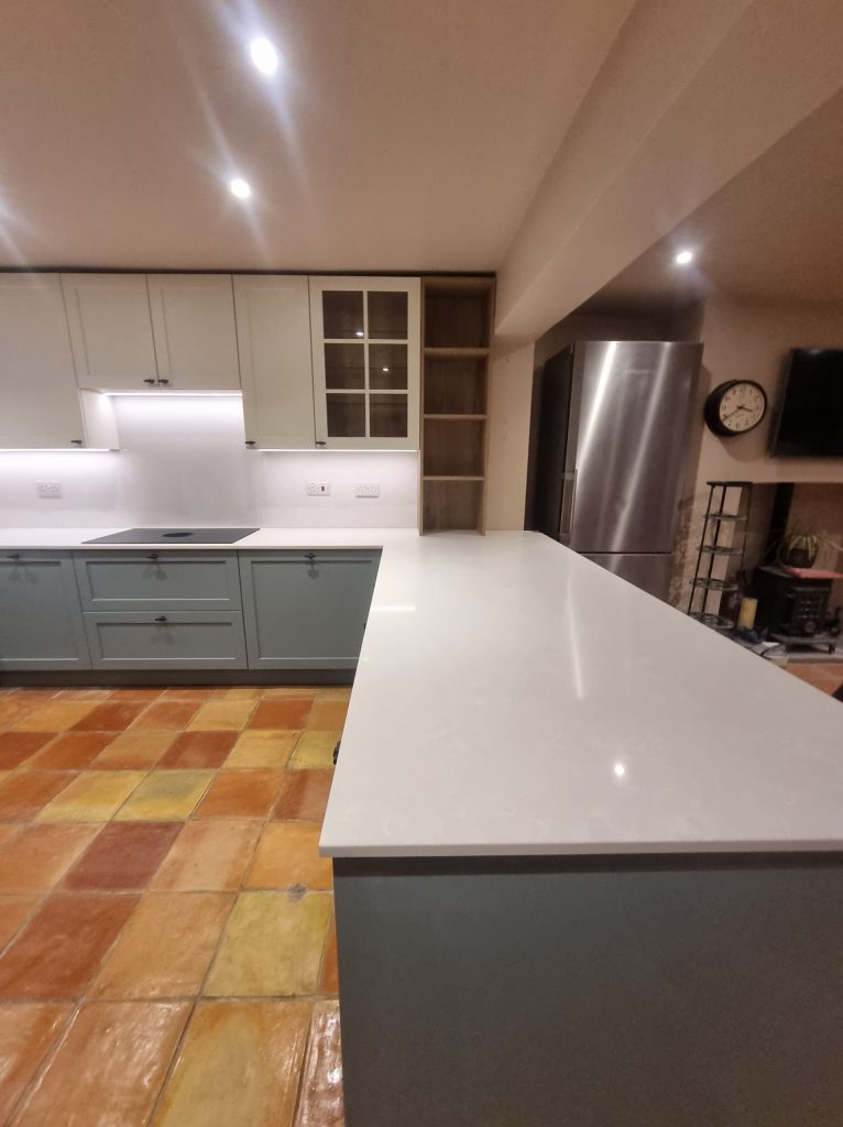 Wide kitchen shot showing worktop detail, soft green base units and pale wall cabinets, Victoria Kitchens